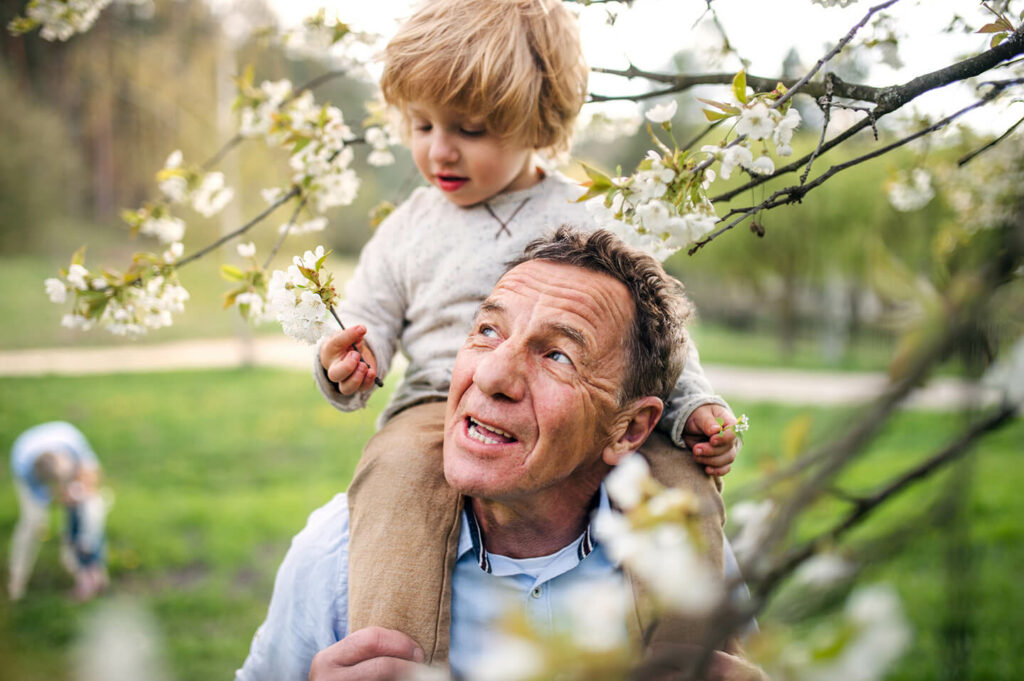 man with child on shoulders looking up standing under tree