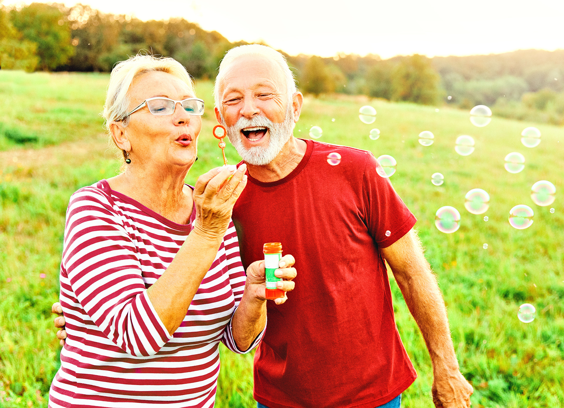 Older couple blowing bubbles in a grass field